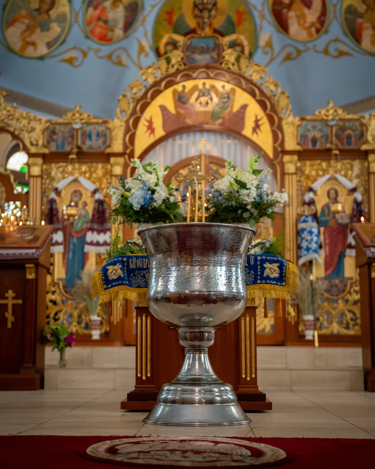 Interior sanctuary of Assumption of the Virgin Mary Church in Northampton, PA with hammered silver font, floral wreaths, and ornate gilded iconostasis