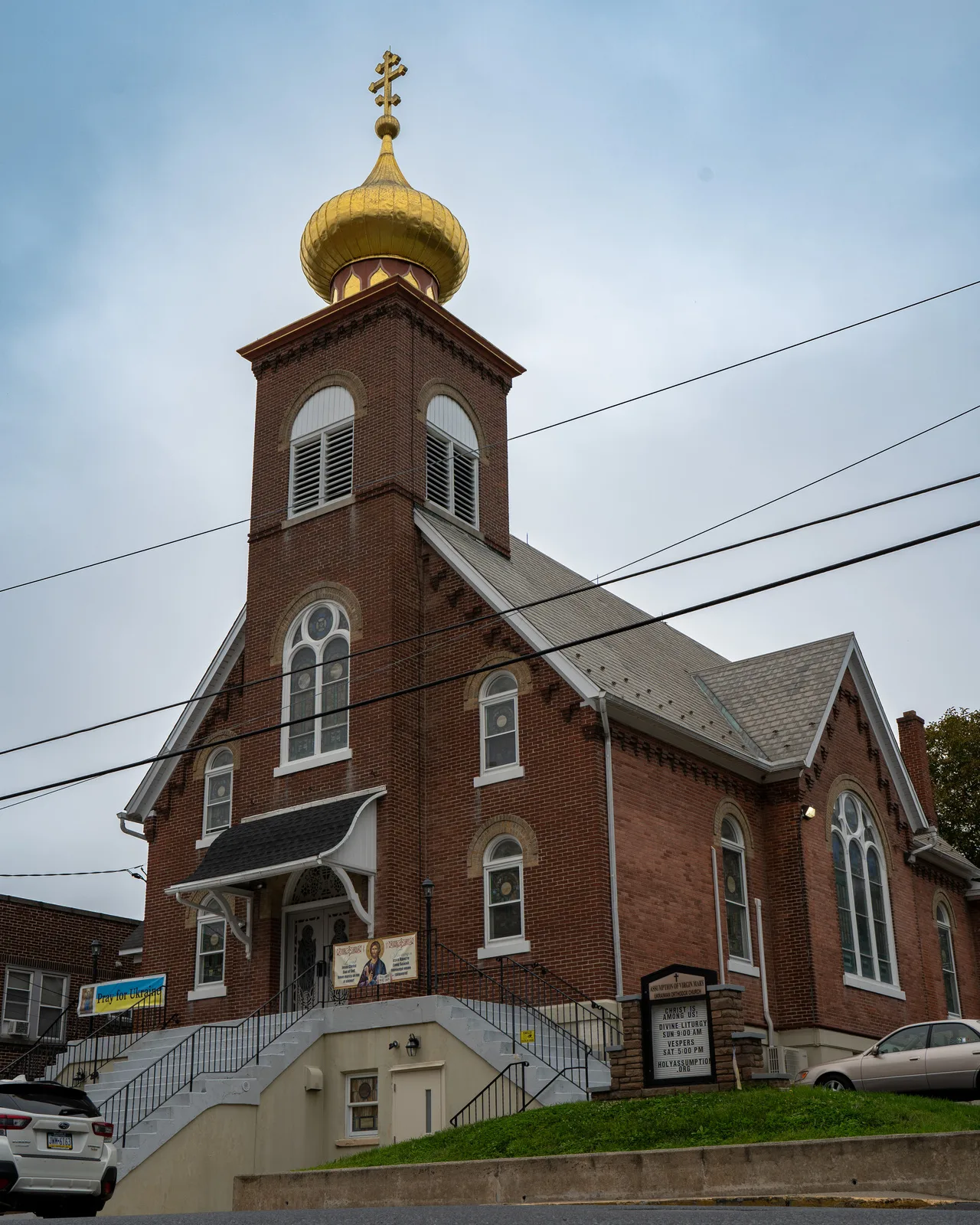 Red-brick exterior of Assumption of the Virgin Mary Ukrainian Orthodox Church in Northampton, PA with towering golden dome and Pray for Ukraine banner